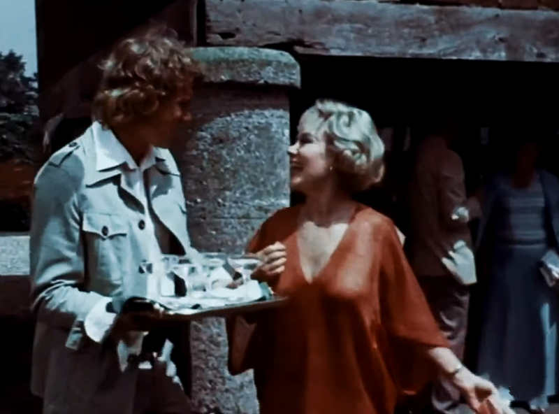 David chats with Mrs. Amworth at the garden party Mrs. Amworth (Glynis Johns) and David (Pip Miller) at the garden party.